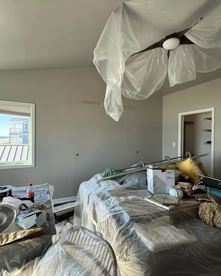 Room with furniture and ceiling fan wrapped in plastic before painting